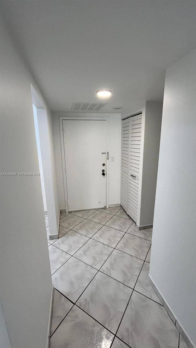 600 Three Islands Boulevard, #913, Hallandale Beach, Hallandale Beach, FL 33009 Entryway featuring large-format ceramic tile flooring, a white metal entry door with a deadbolt, and a built-in closet with louvered bi-fold doors