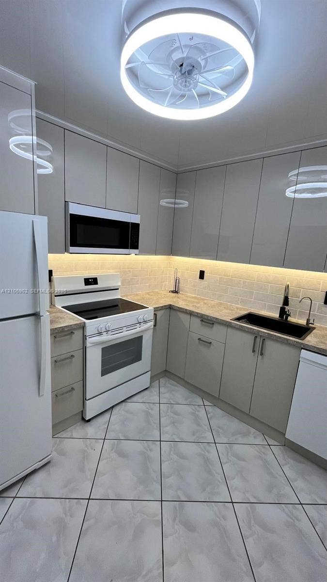 600 Three Islands Boulevard, #913, Hallandale Beach, Hallandale Beach, FL 33009 Kitchen featuring high-gloss cabinetry, stone-patterned countertops, a subway tile backsplash with under-cabinet lighting, a built-in microwave, and a flush-mount circular ceiling fixture