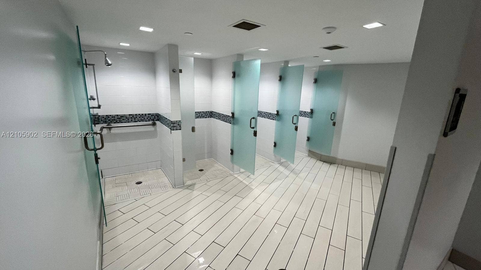 600 Three Islands Boulevard, #913, Hallandale Beach, Hallandale Beach, FL 33009 Multiple individual shower stalls featuring frosted glass doors, white tiled flooring, inset decorative wall tiling, and recessed ceiling lighting