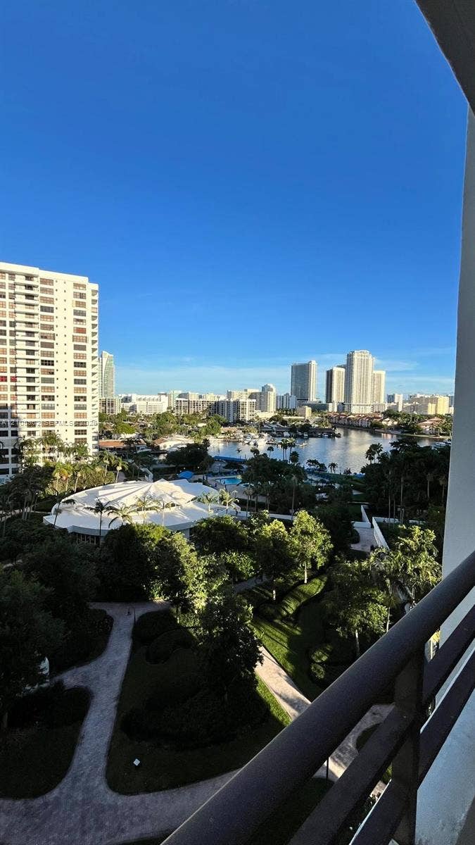 600 Three Islands Boulevard, #913, Hallandale Beach, Hallandale Beach, FL 33009 Elevated terrace with a metal railing overlooking a landscape of mature trees, paved pathways, and a waterfront cityscape