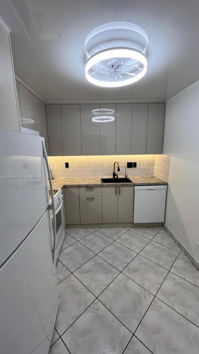 600 Three Islands Boulevard, #913, Hallandale Beach, Hallandale Beach, FL 33009 Kitchen featuring flat-panel cabinetry, light-toned tiled flooring, a brick-pattern backsplash, under-cabinet lighting, and a modern circular LED flush-mount fixture