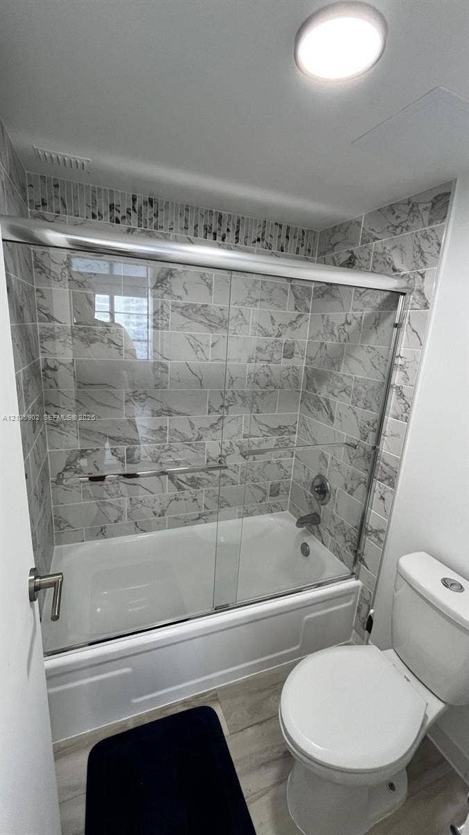 600 Three Islands Boulevard, #913, Hallandale Beach, Hallandale Beach, FL 33009 Bathroom featuring a soaking tub with a glass sliding enclosure, floor-to-ceiling stone-finish tile surround, wood-finish flooring, and a flush-mount ceiling light fixture