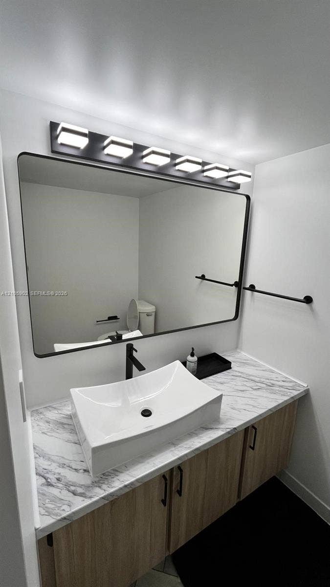 600 Three Islands Boulevard, #913, Hallandale Beach, Hallandale Beach, FL 33009 Floating vanity with wood-finish cabinetry, stone-patterned countertop, rectangular vessel sink, matte black faucet, and modern multi-light fixture