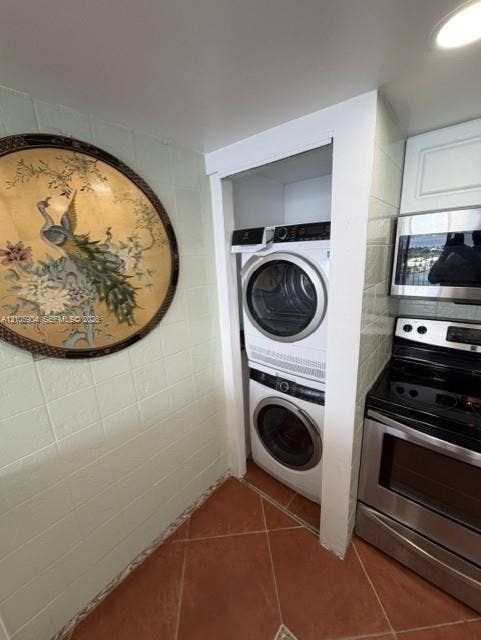 7601 E Treasure Drive, #2417, North Bay Village, North Bay Village, FL 33141 Stacked front-loading laundry appliances, stainless steel microwave, and stainless steel electric range, featuring tiled wall surfaces and terracotta-style floor tiling