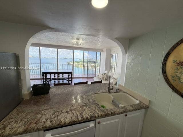 7601 E Treasure Drive, #2417, North Bay Village, North Bay Village, FL 33141 Kitchen featuring stone countertops, a dual-basin undermount sink, white cabinetry, and an arched pass-through opening to a balcony with water scenery