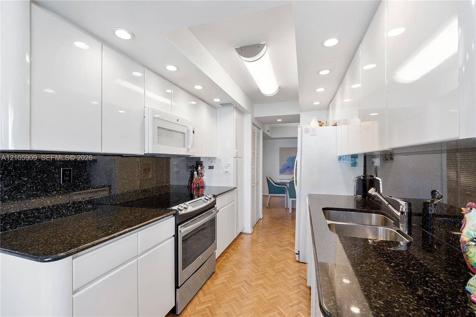 Kitchen featuring high-gloss white cabinetry, dark stone countertops, stainless steel appliances, recessed ceiling lighting, and parquet wood-finish flooring