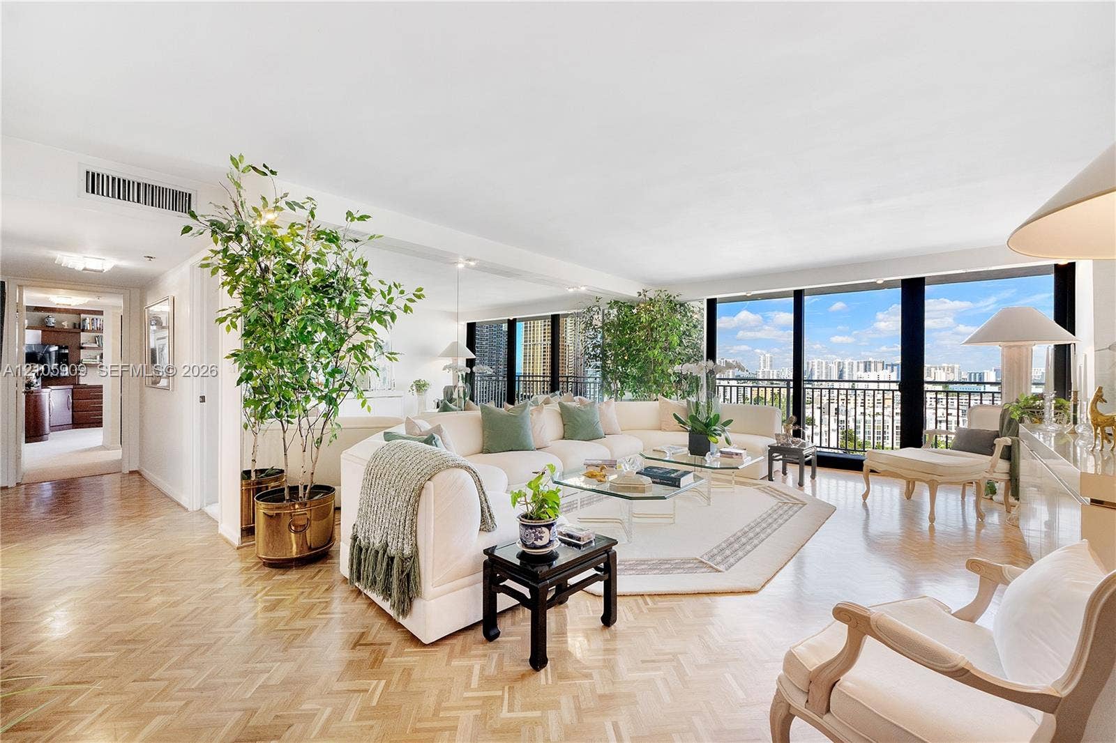 Expansive living area featuring herringbone-pattern wood flooring, floor-to-ceiling windows, an integrated mirrored wall, and a private balcony