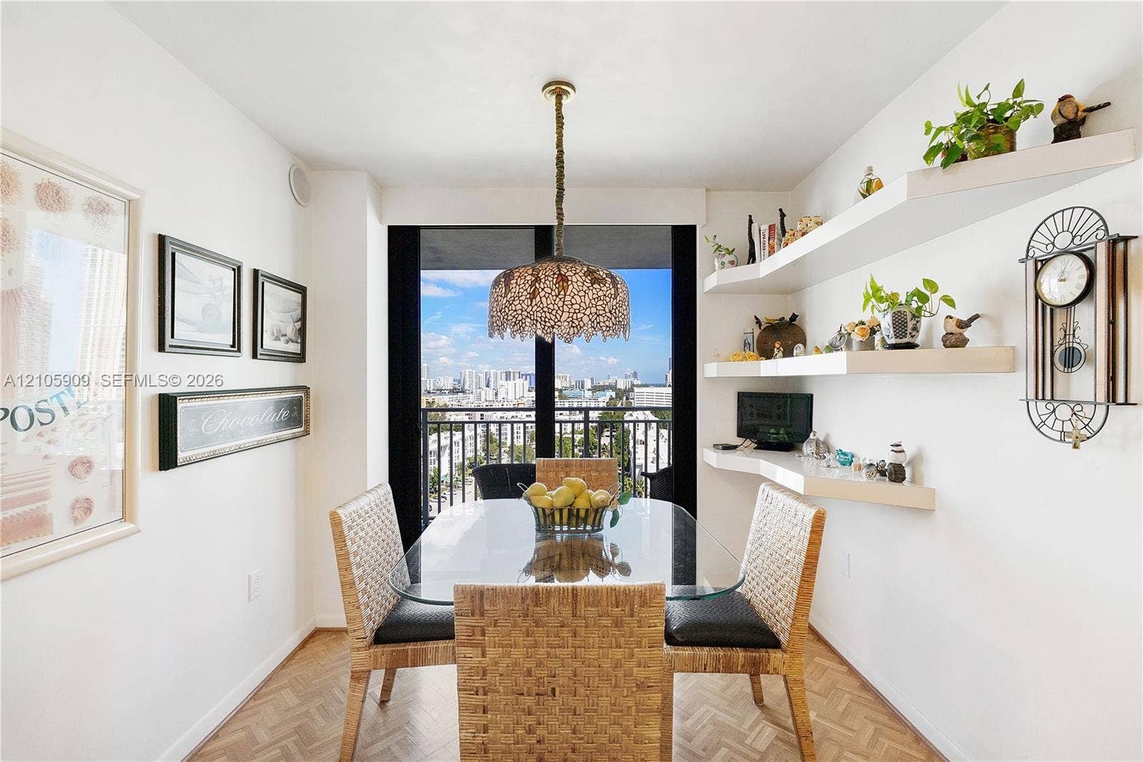 Dining area featuring parquet wood-finish flooring, decorative ceiling pendant lighting, custom white floating shelving, and floor-to-ceiling glass sliding doors opening to a balcony
