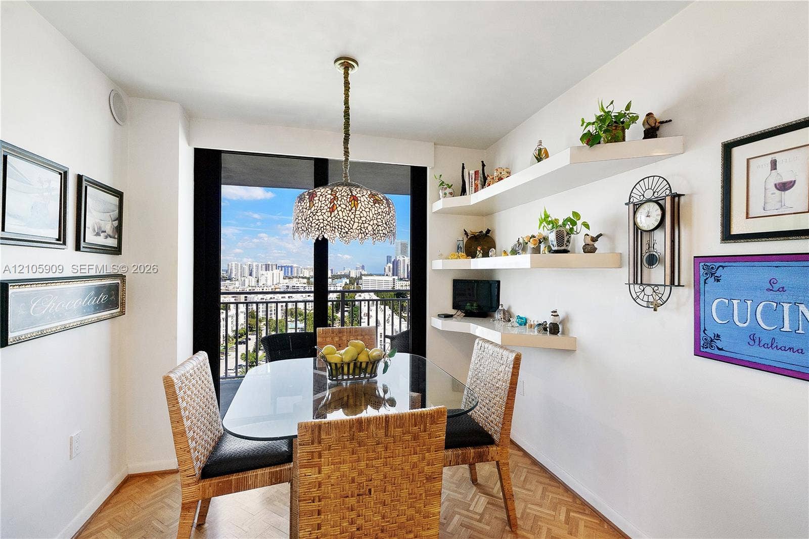 Dining space featuring herringbone patterned wood-finish flooring, a decorative pendant light fixture, built-in floating wall shelving, and floor-to-ceiling glass sliding doors leading to a balcony