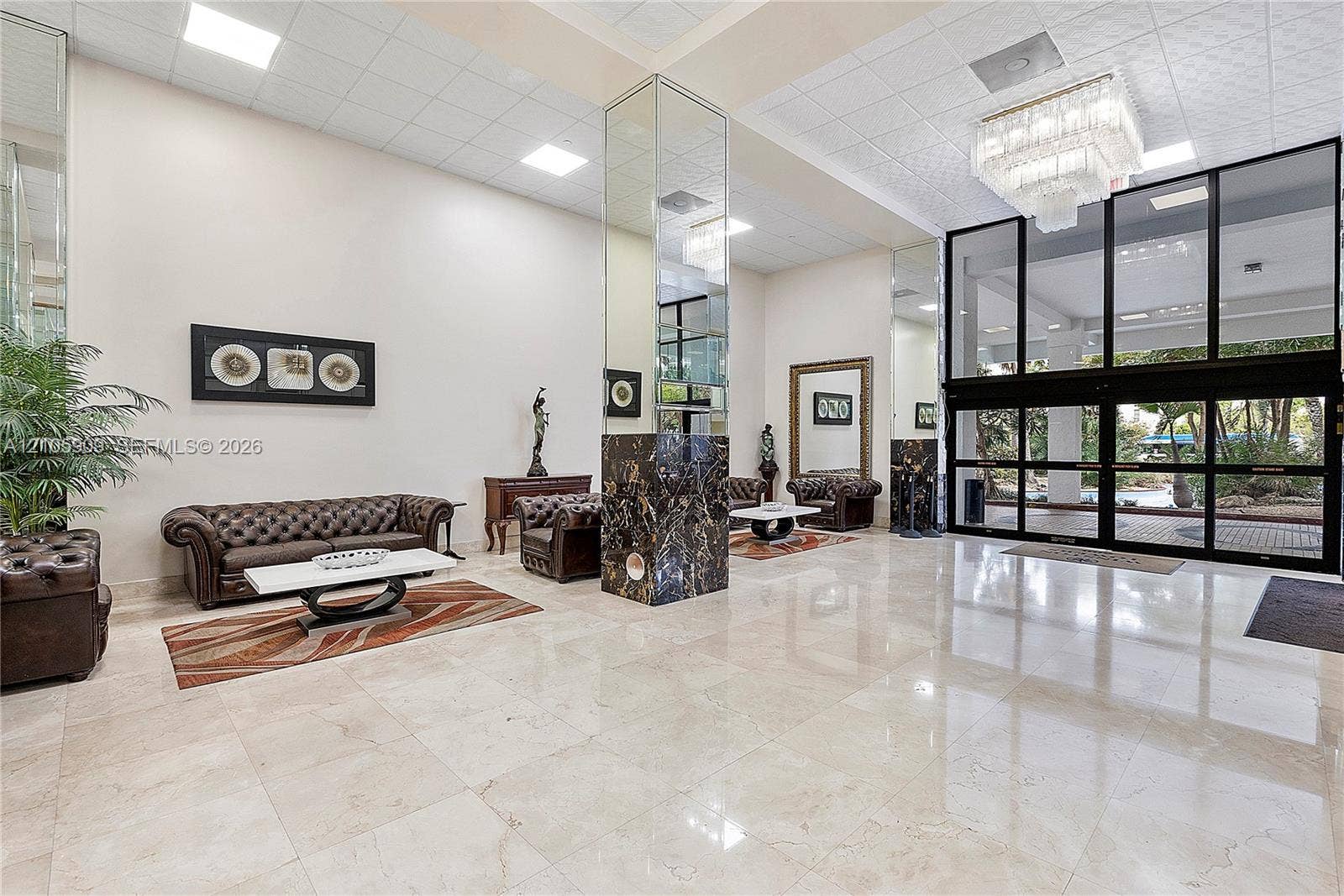 Grand lobby entrance featuring polished stone flooring, dark stone-clad columns, floor-to-ceiling glass panel doors, and a multi-tiered crystal chandelier