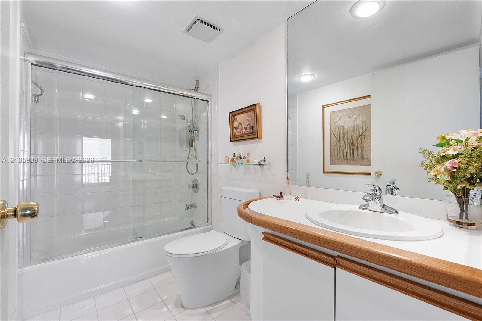Full-width mirror, white cabinetry with wood-finish trim, integrated vanity countertop with undermount basin, and a shower-tub combination featuring a sliding glass enclosure