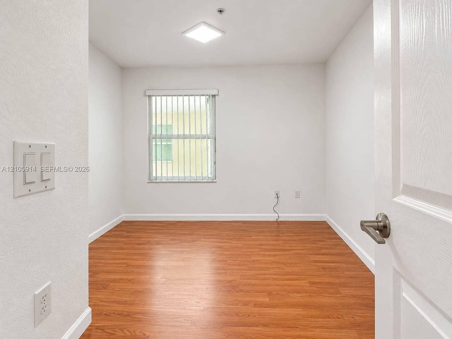 11102 NW 83rd Street, #216, Doral, FL 33178 Room featuring wood-finish flooring, a flush-mount light fixture, and a window with vertical blinds