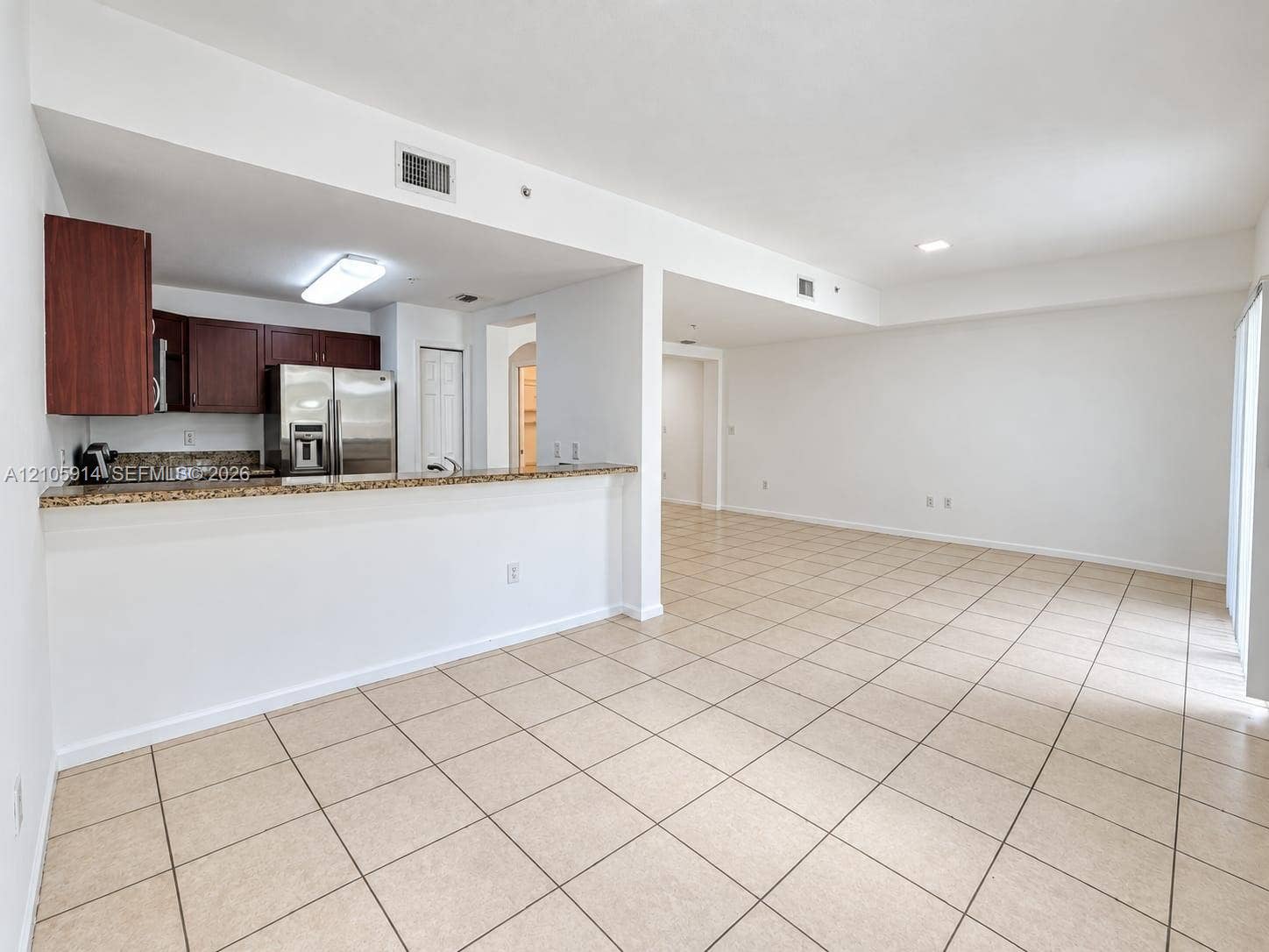 11102 NW 83rd Street, #216, Doral, FL 33178 Kitchen featuring a breakfast bar with stone-finish countertops, dark wood cabinetry, and stainless steel refrigerator, complemented by neutral tile flooring throughout the interior