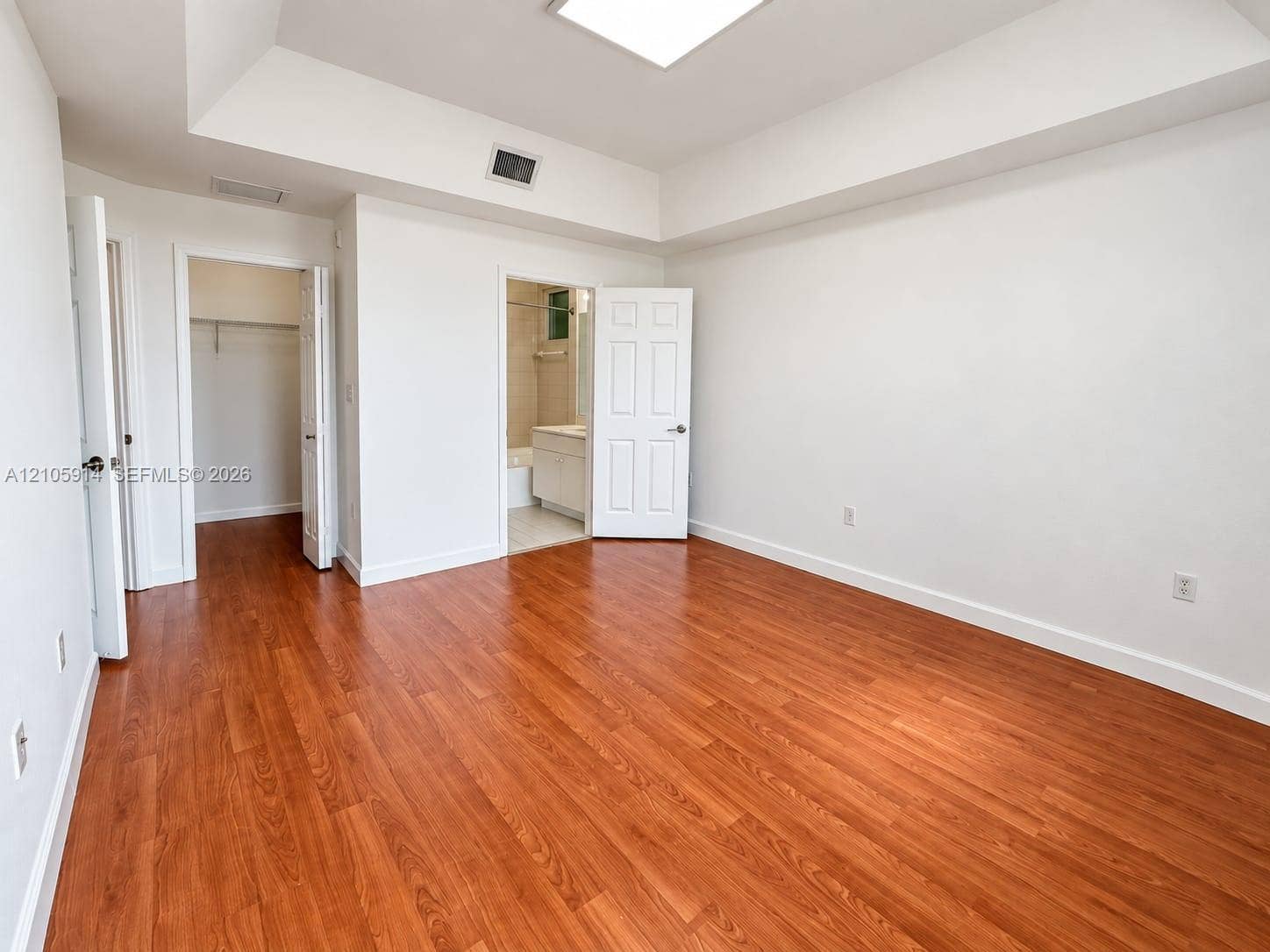11102 NW 83rd Street, #216, Doral, FL 33178 Room featuring wood-finish flooring, a tray ceiling, recessed lighting, and dual entry points to a walk-in closet and an en-suite bathroom