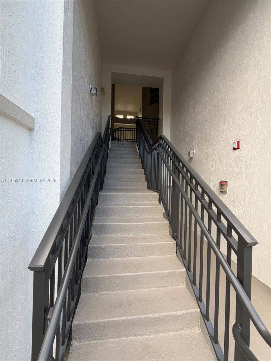 11102 NW 83rd Street, #216, Doral, FL 33178 Staircase featuring concrete steps, dual dark-finish metal handrails, and textured wall surfaces