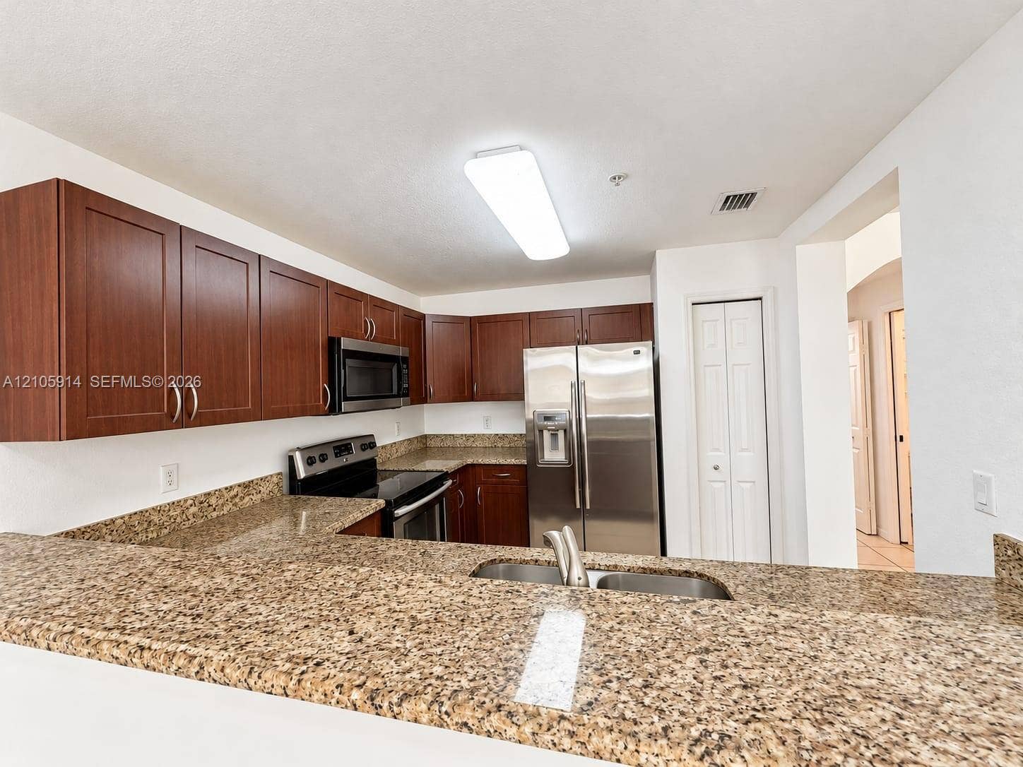 11102 NW 83rd Street, #216, Doral, FL 33178 Kitchen featuring stained wood cabinetry, stone-surface countertops, stainless steel appliances, dual-basin sink, and integrated breakfast bar