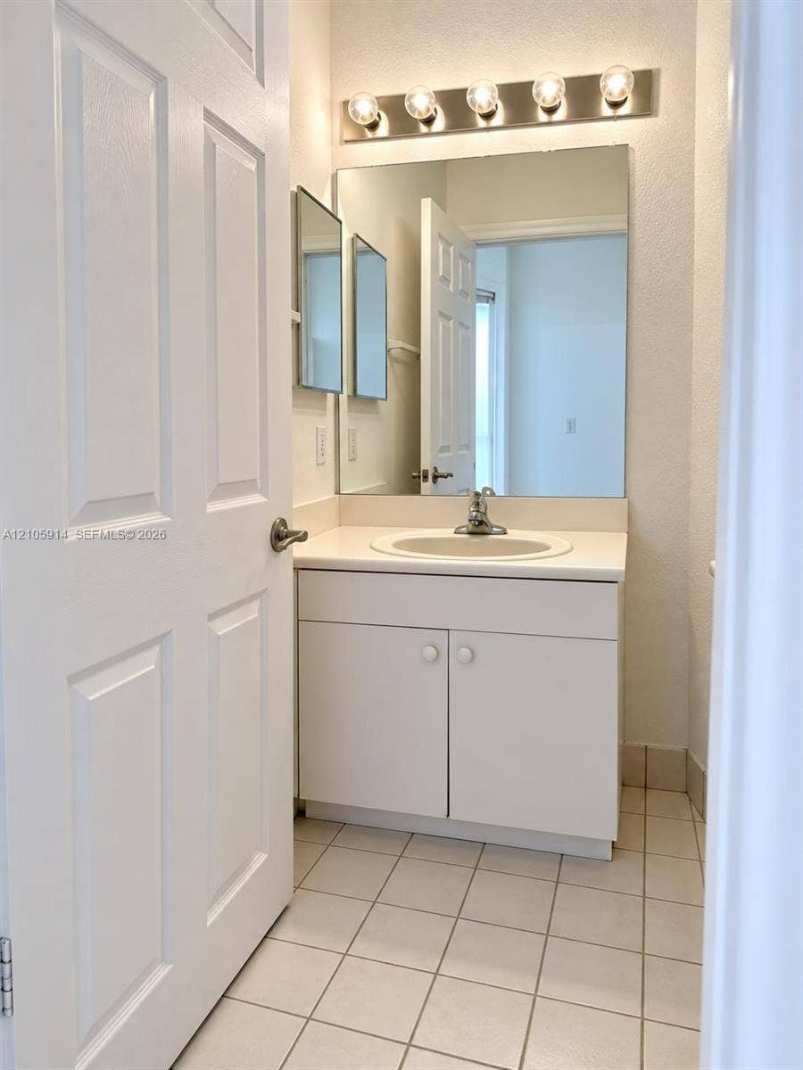 11102 NW 83rd Street, #216, Doral, FL 33178 Vanity cabinet with a white countertop and integrated sink, wall-mounted mirror, five-light fixture, and ceramic tile flooring