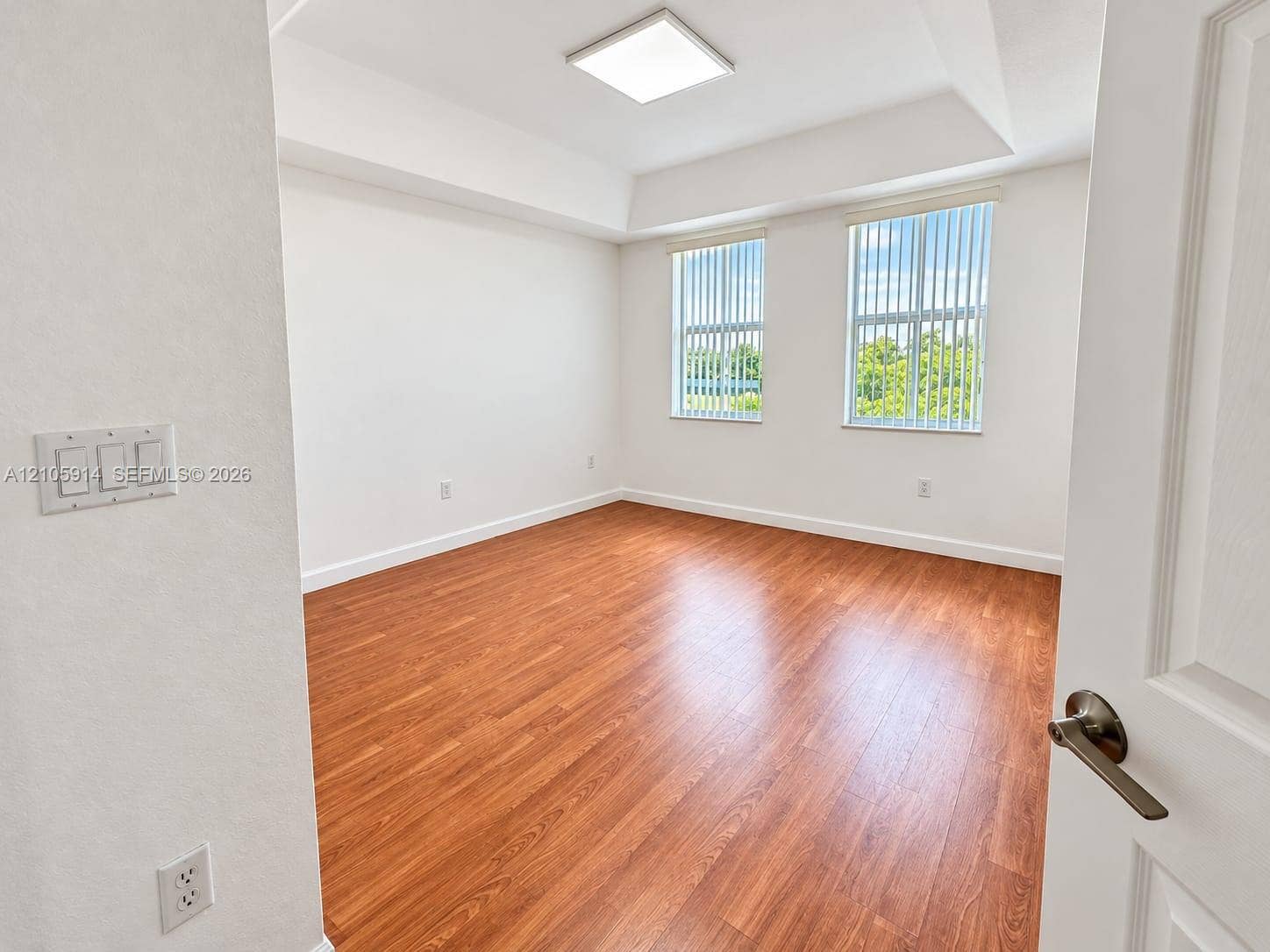 11102 NW 83rd Street, #216, Doral, FL 33178 Room featuring wood-finish flooring, a tray ceiling, dual vertical windows, and a flush-mount overhead light fixture