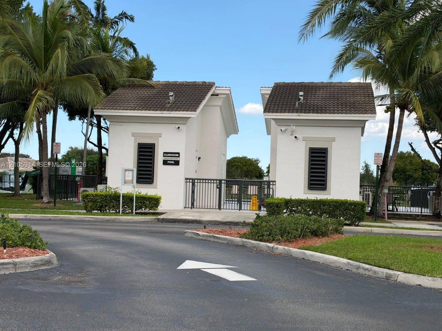 11102 NW 83rd Street, #216, Doral, FL 33178 Gated entry featuring dual stucco structures, tile roofing, and metal security fencing surrounded by manicured landscaping and palm trees