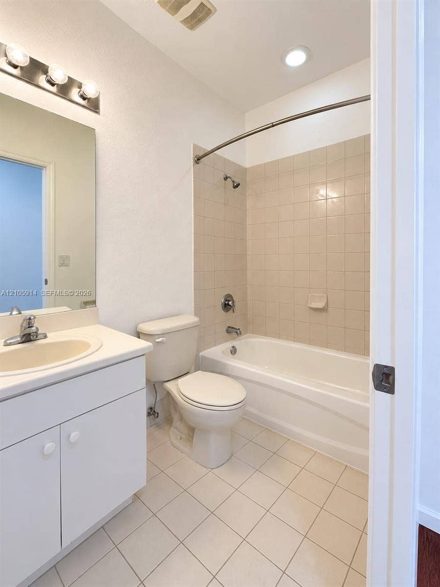 11102 NW 83rd Street, #216, Doral, FL 33178 Bathroom featuring a white vanity cabinet, solid-surface countertop with an integrated sink, tiled tub surround, and a curved shower curtain rod
