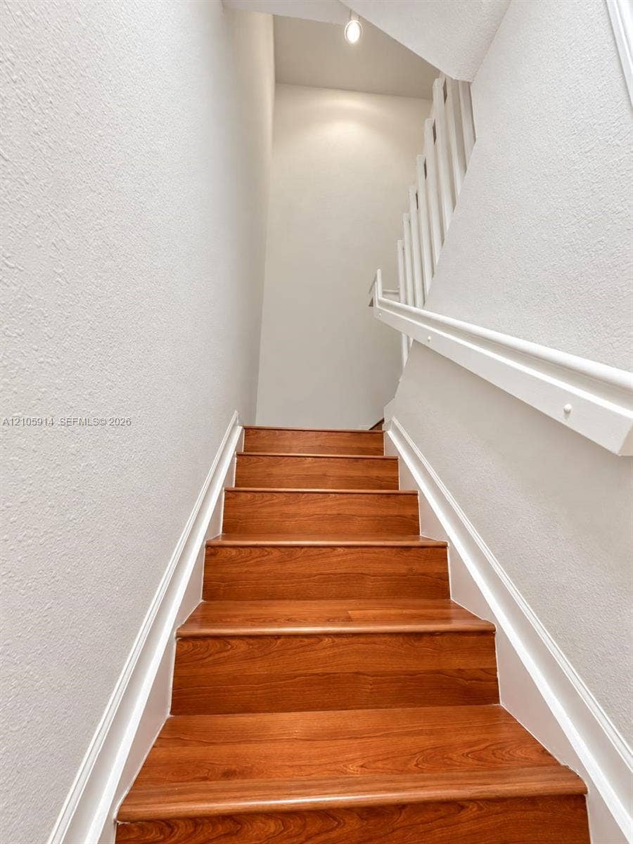 11102 NW 83rd Street, #216, Doral, FL 33178 Staircase featuring wood-finish treads, white painted walls, and a white handrail with vertical balusters