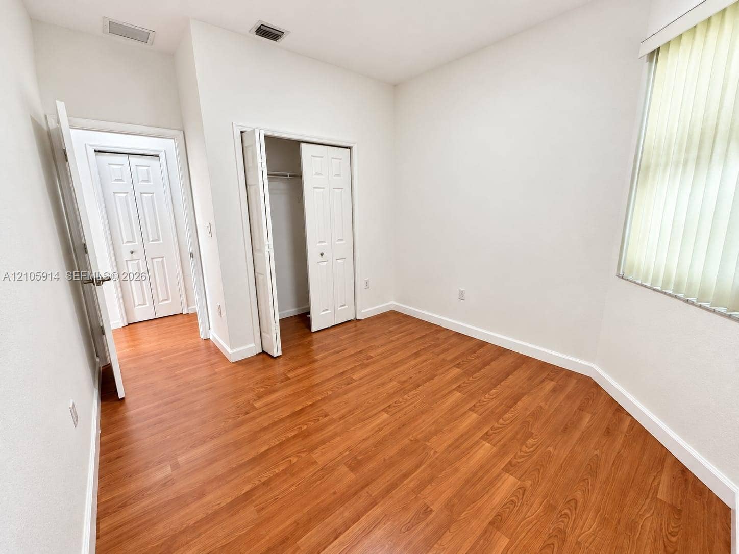 11102 NW 83rd Street, #216, Doral, FL 33178 Room featuring wood-finish flooring, white walls, vertical window blinds, and dual bi-fold door closets