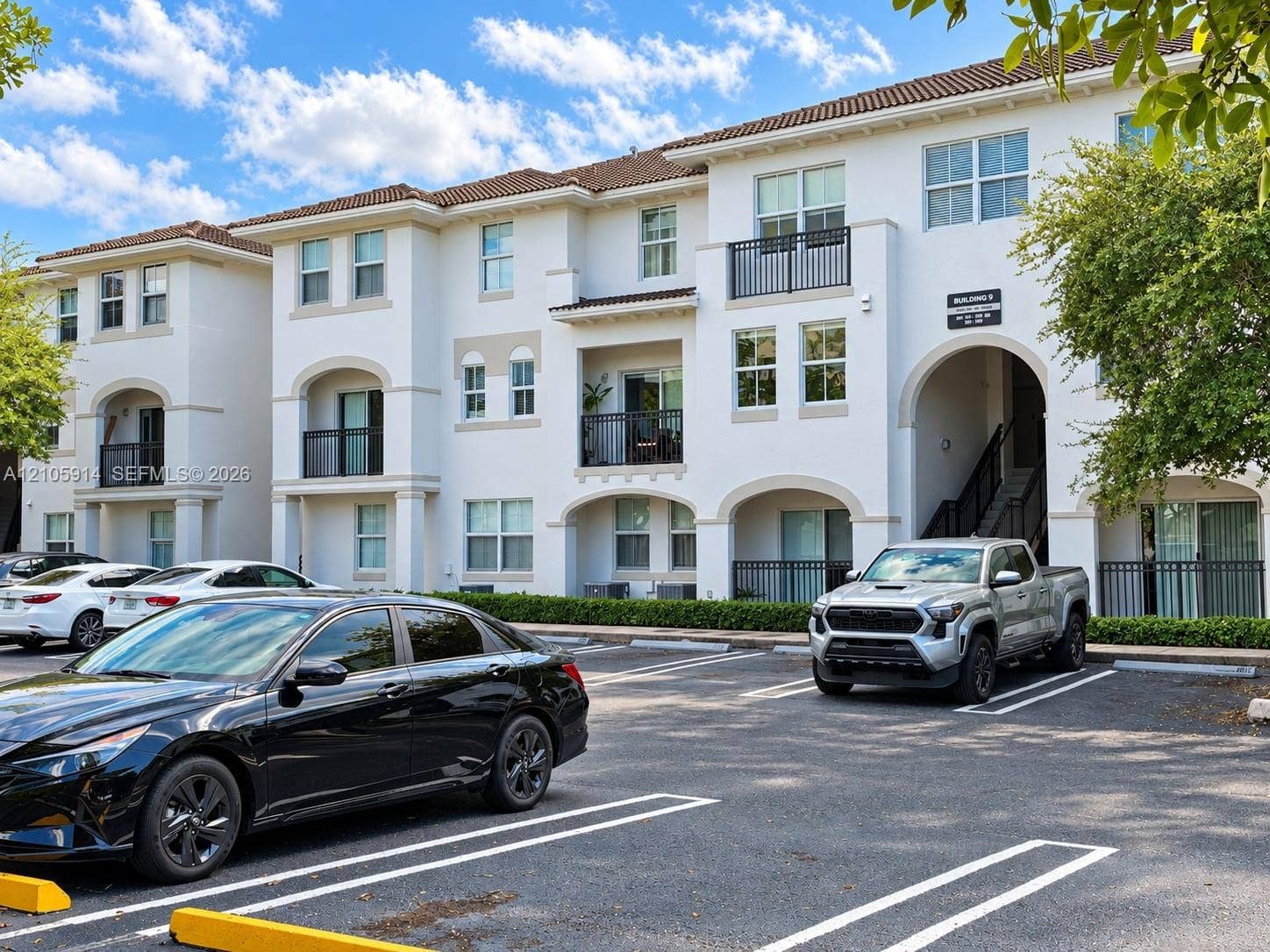 11102 NW 83rd Street, #216, Doral, FL 33178 Multi-story stucco exterior featuring arched architectural detailing, tile roof, private balconies with metal railings, and surface parking
