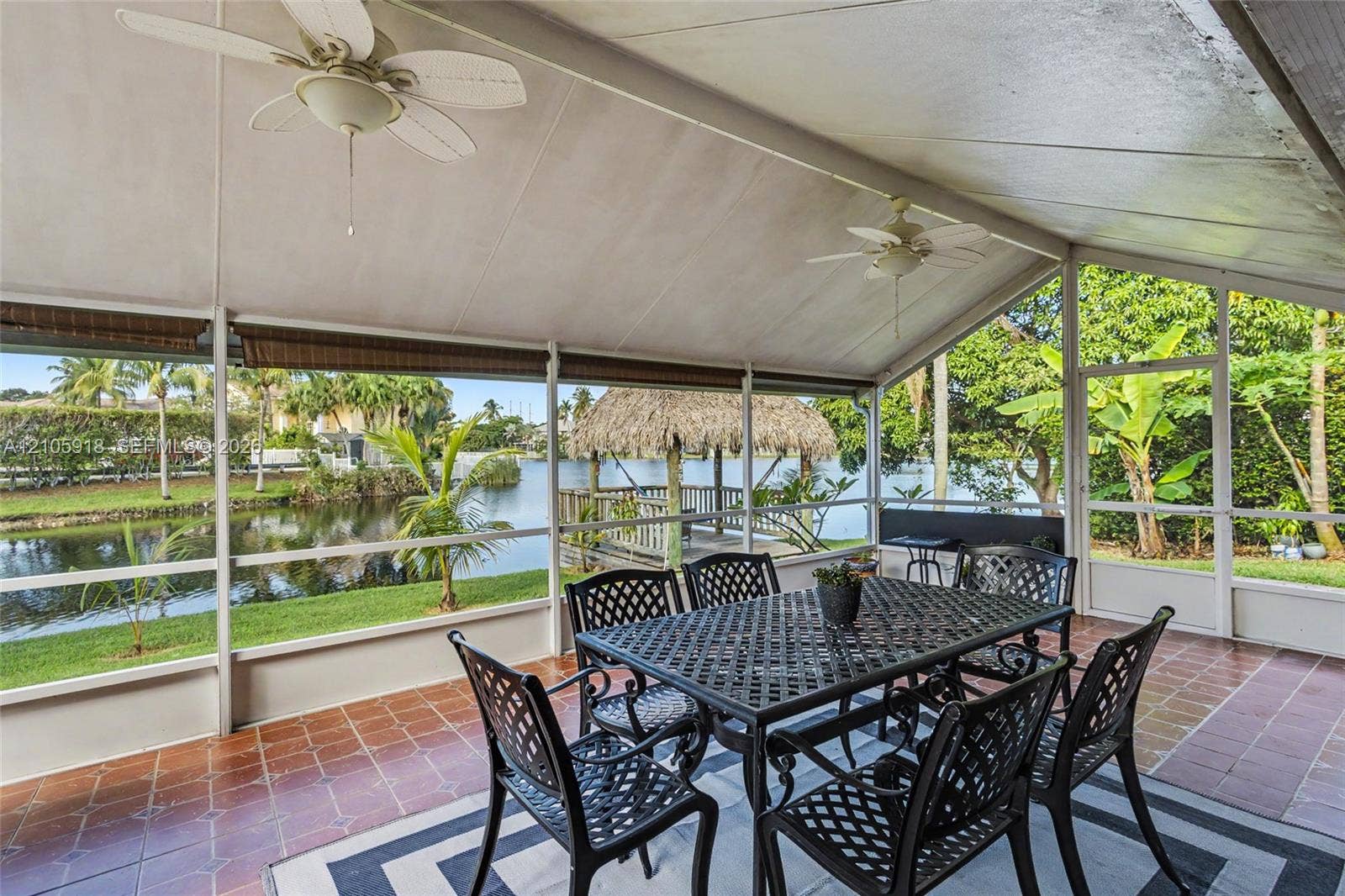 Screened-in patio featuring tiled flooring, dual ceiling fans, and a water-facing structure with a thatched roof