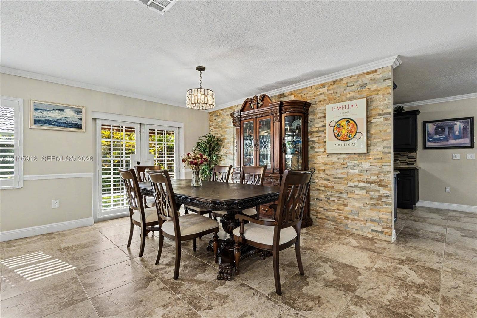 Stacked stone accent wall, large-format tile flooring, French doors with integrated plantation shutters, and tiered crystal drum chandelier