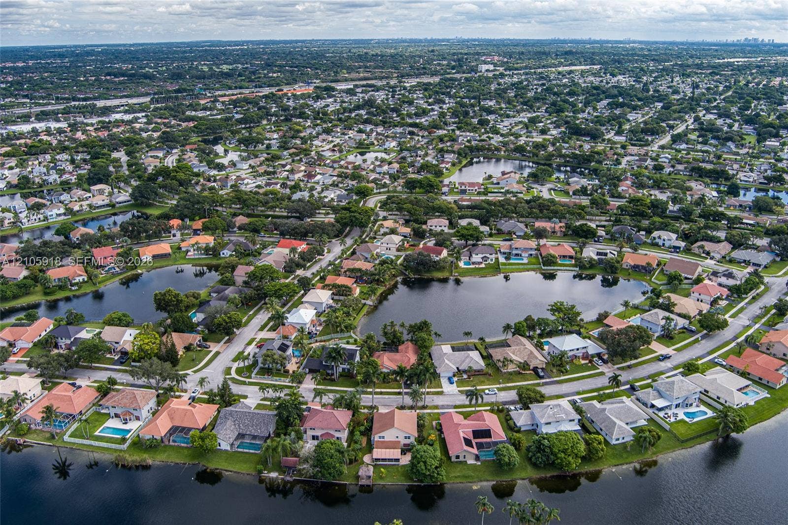 Aerial perspective of a residential community featuring winding paved streets, single-family dwellings with tile roofing, mature landscaping, and multiple waterfront lots