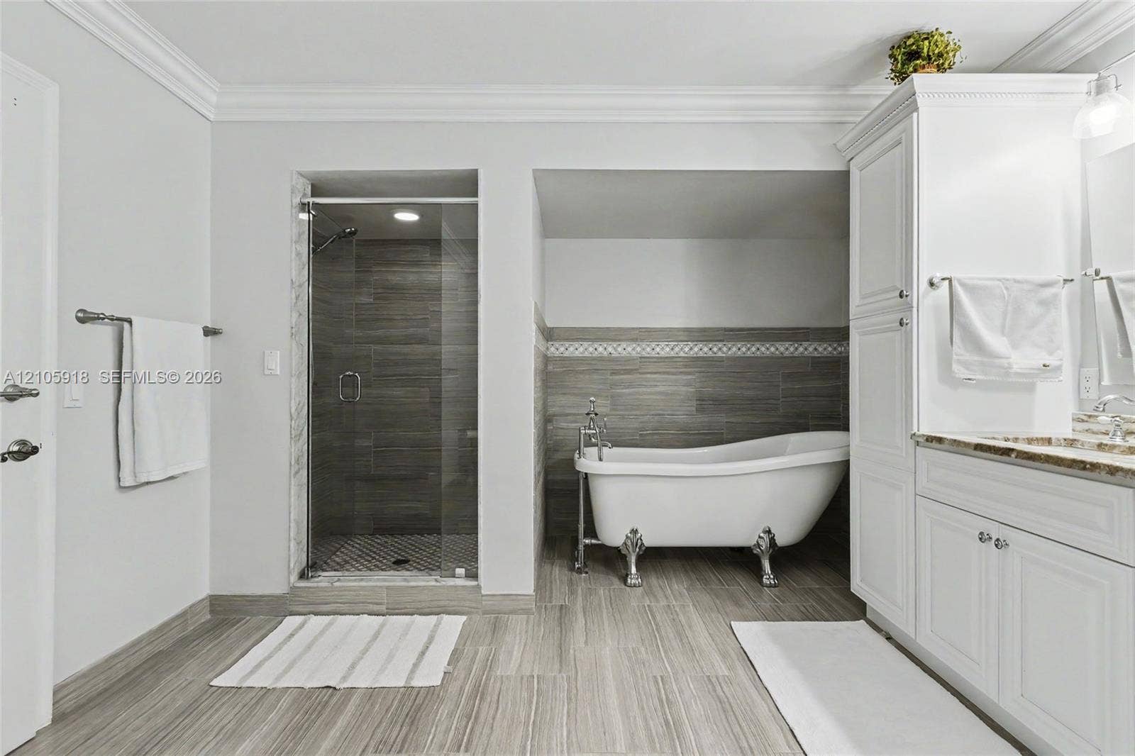 Freestanding clawfoot tub, walk-in shower with glass enclosure, white built-in cabinetry, stone-finish countertops, and neutral tile flooring