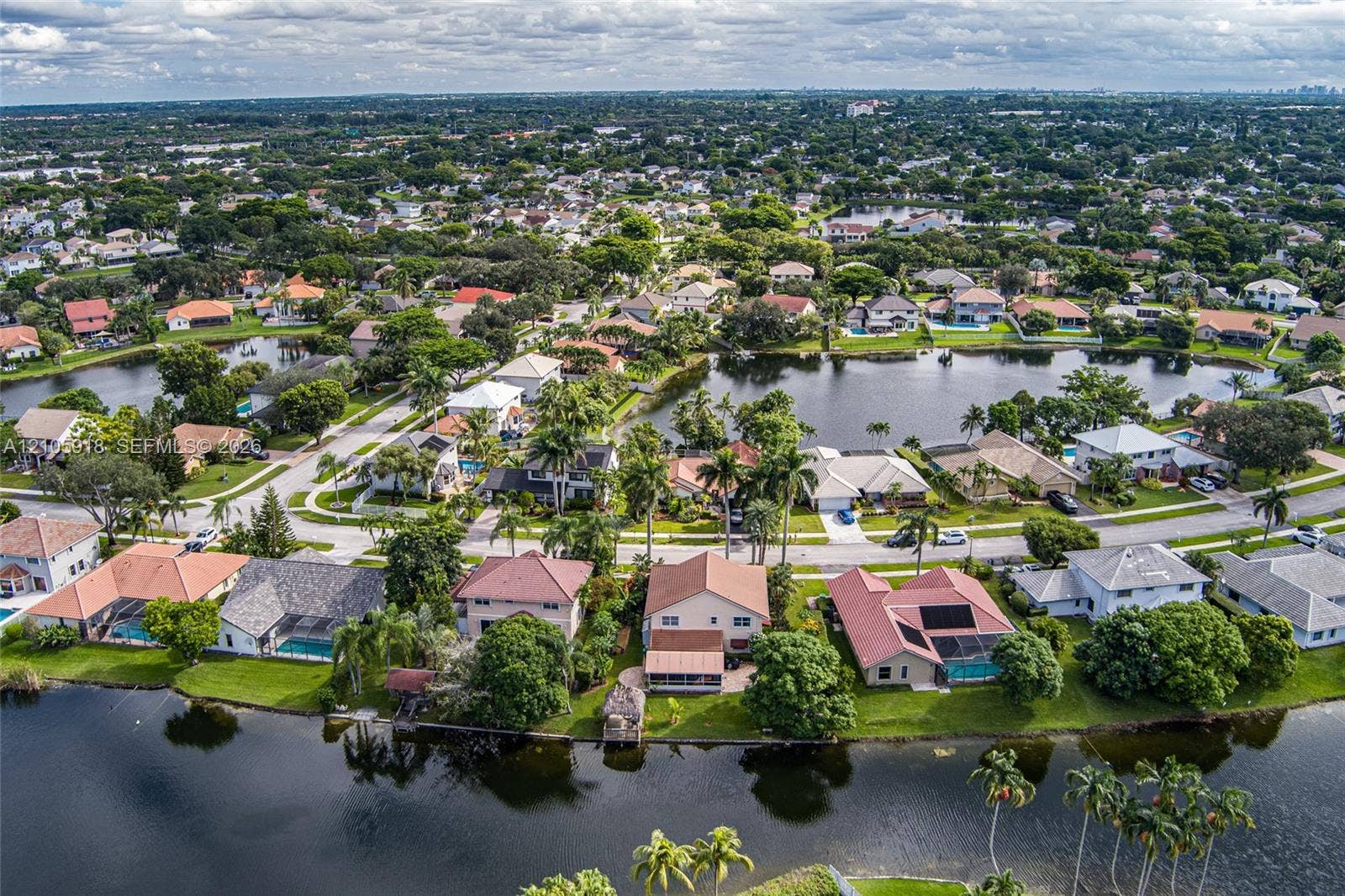 Aerial perspective featuring waterfront property positioning, multiple canal-front lots, mature tropical landscaping, and paved street infrastructure