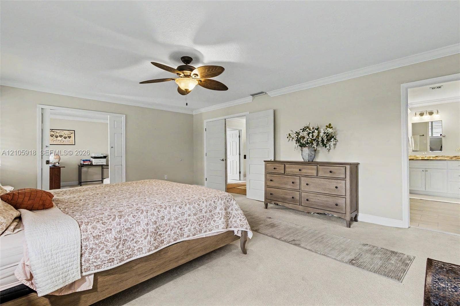Neutral-toned room featuring a ceiling fan with integrated lighting, crown molding, and double-door entry