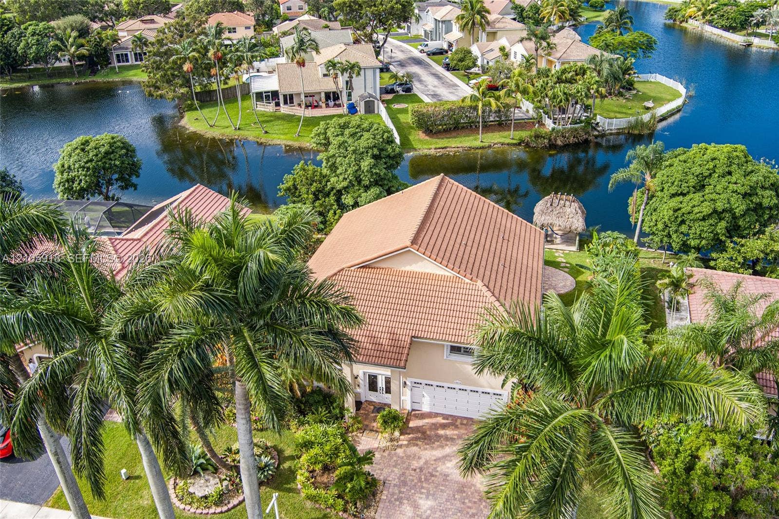 Waterfront property featuring a tile roof, paver driveway, and mature palm trees