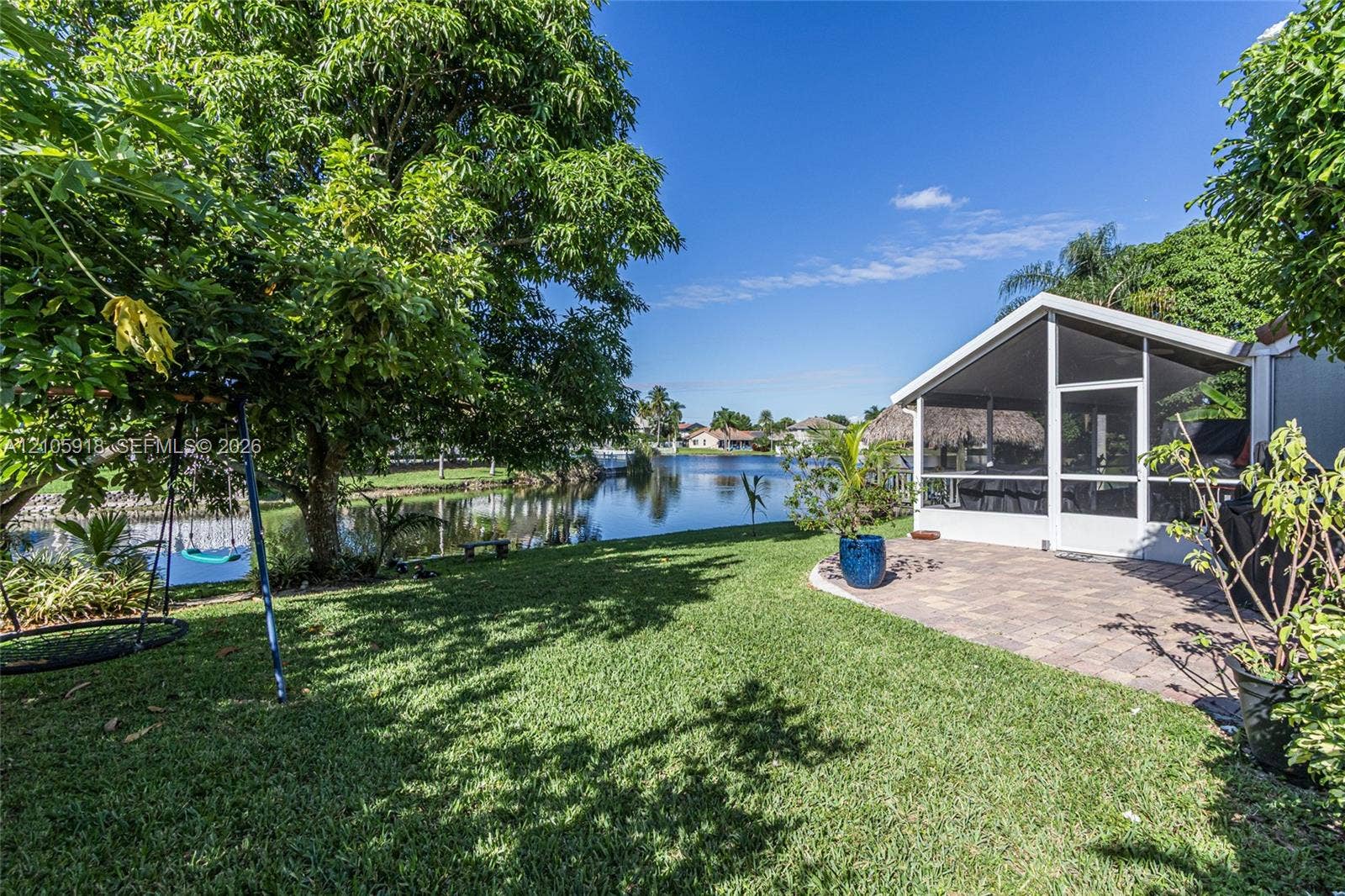 Waterfront backyard featuring a screen-enclosed lanai, paver patio, established landscaping, and mature trees