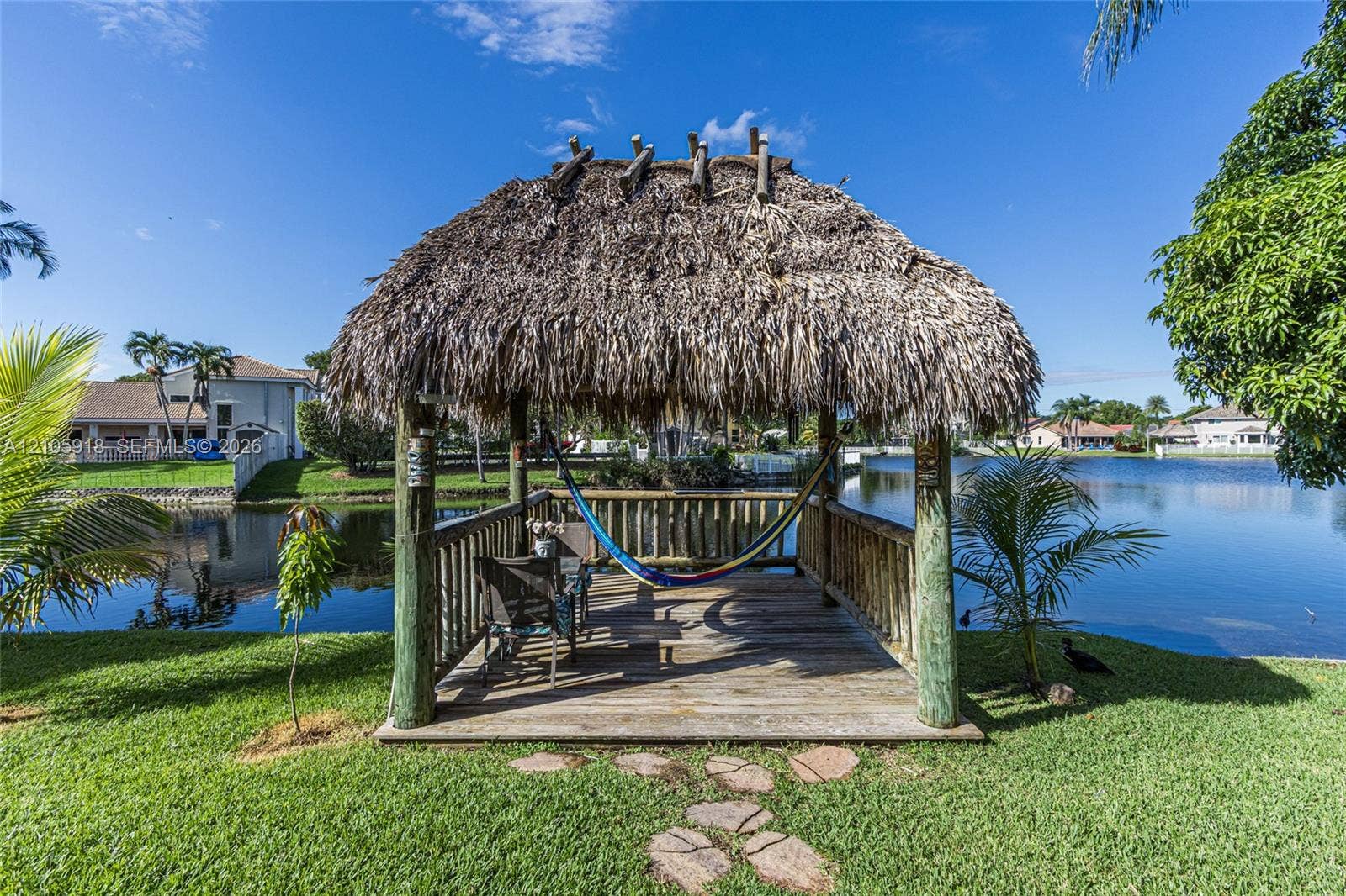 Waterfront tiki-style gazebo featuring a thatched roof, wood-plank decking, and timber posts