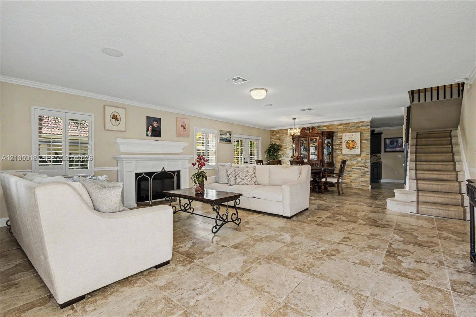 Living area featuring tile flooring, a fireplace with a white mantel, stone-accented wall, and a staircase with a runner