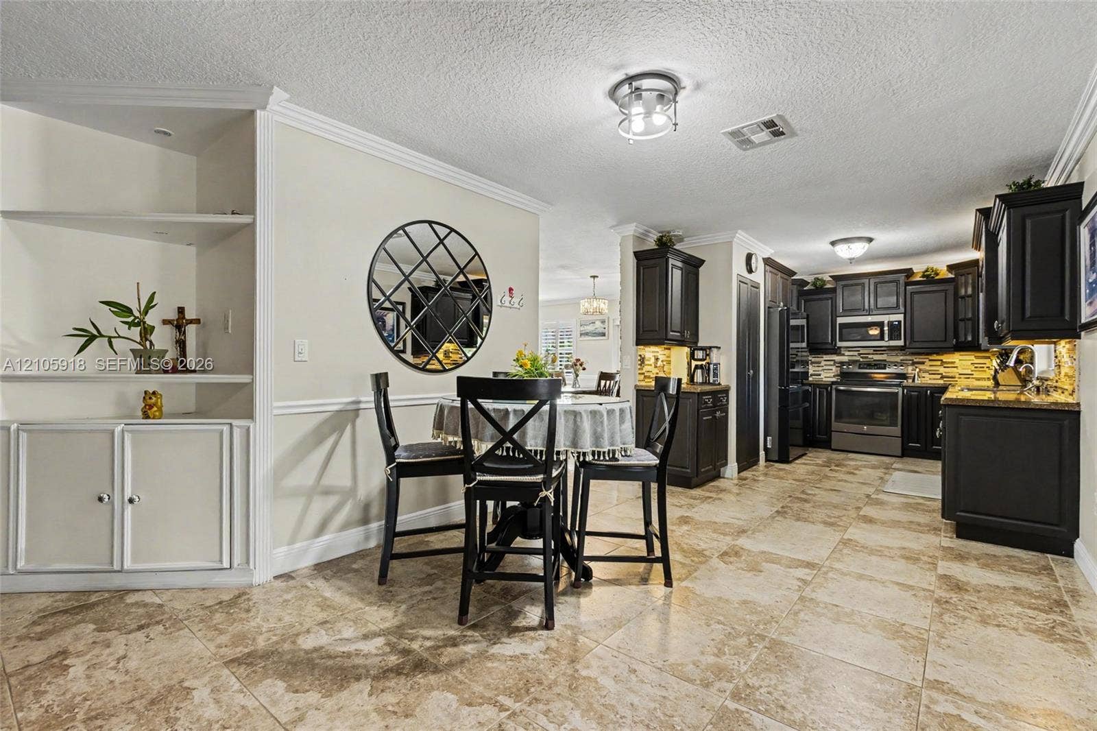 Kitchen featuring dark cabinetry, stone-finish countertops, ceramic tile flooring, and built-in shelving with crown molding