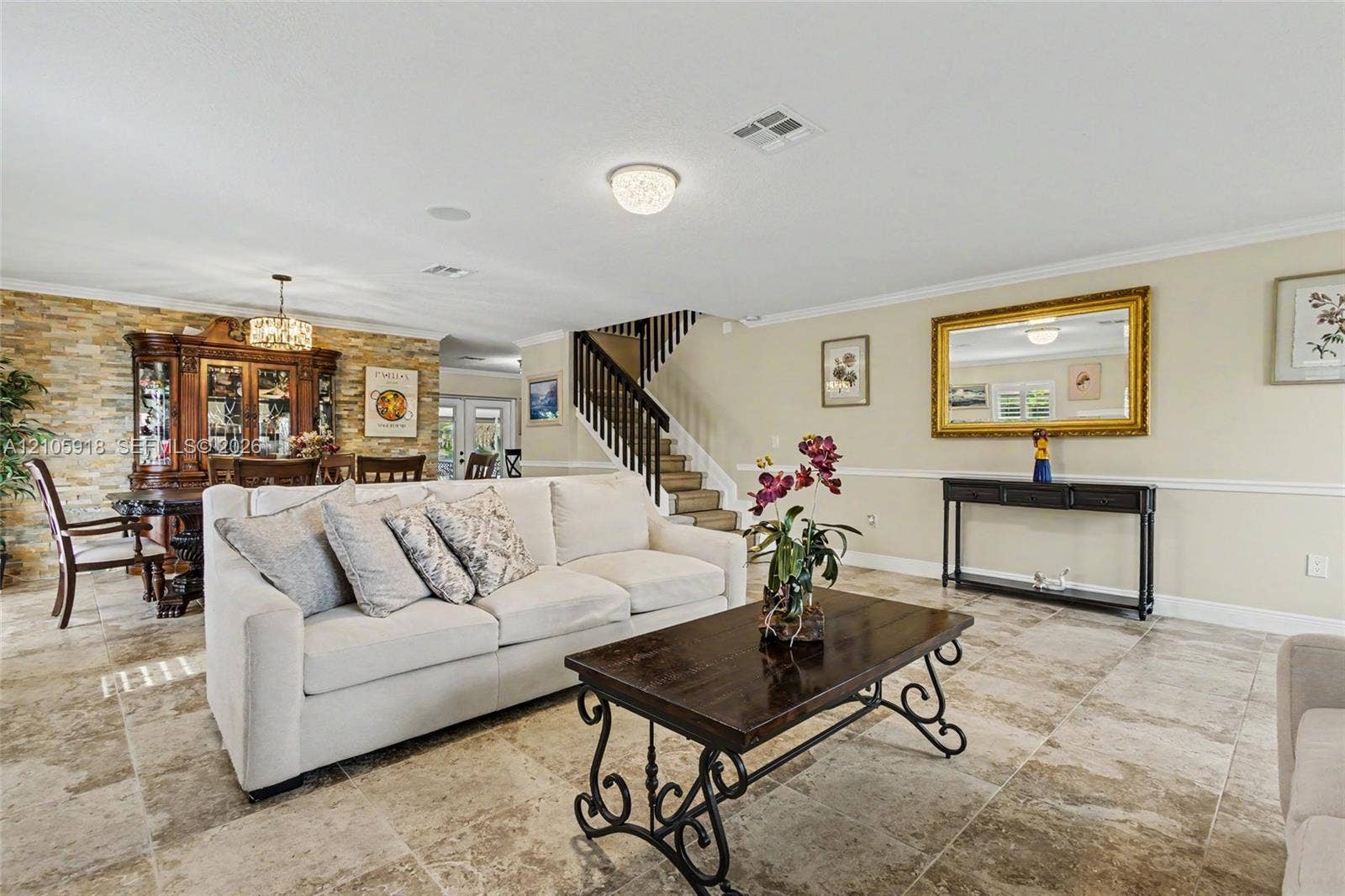 Open-concept interior featuring large-format stone tile flooring, a floor-to-ceiling textured stone accent wall, chair rail molding, and a staircase with decorative wrought iron railing