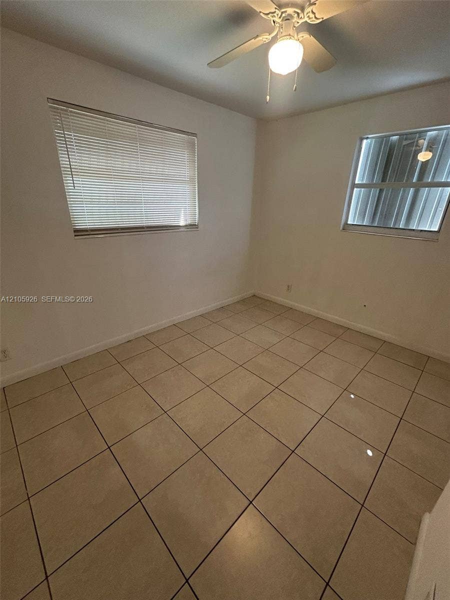 1601 W Avenue H W, Riviera Beach, Riviera Beach, FL 33404 Interior room featuring large-format ceramic tile flooring, neutral wall finishes, multi-pane windows with horizontal blinds, and a central ceiling fan with an integrated light fixture