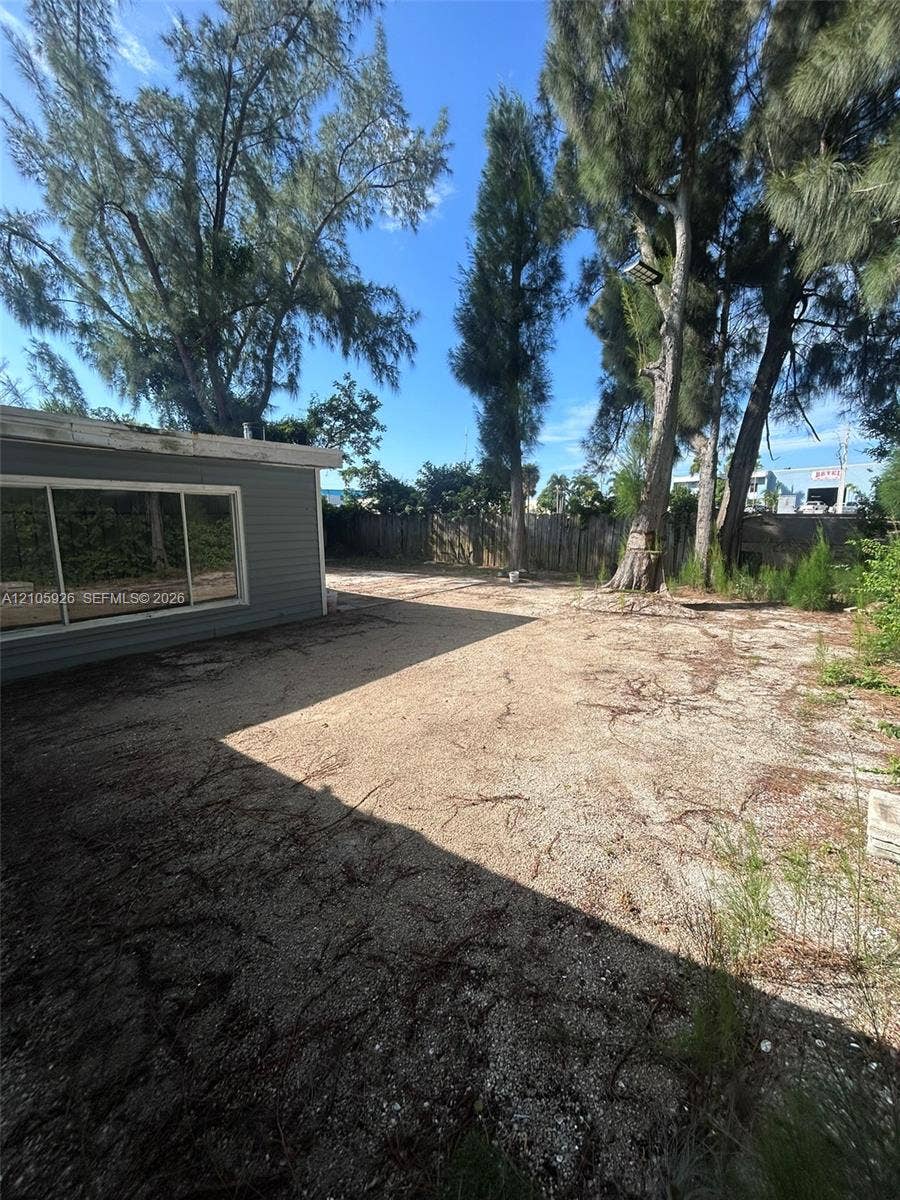 1601 W Avenue H W, Riviera Beach, Riviera Beach, FL 33404 Outdoor space featuring gray horizontal siding, large windows with white trim, mature trees, and wooden perimeter fencing