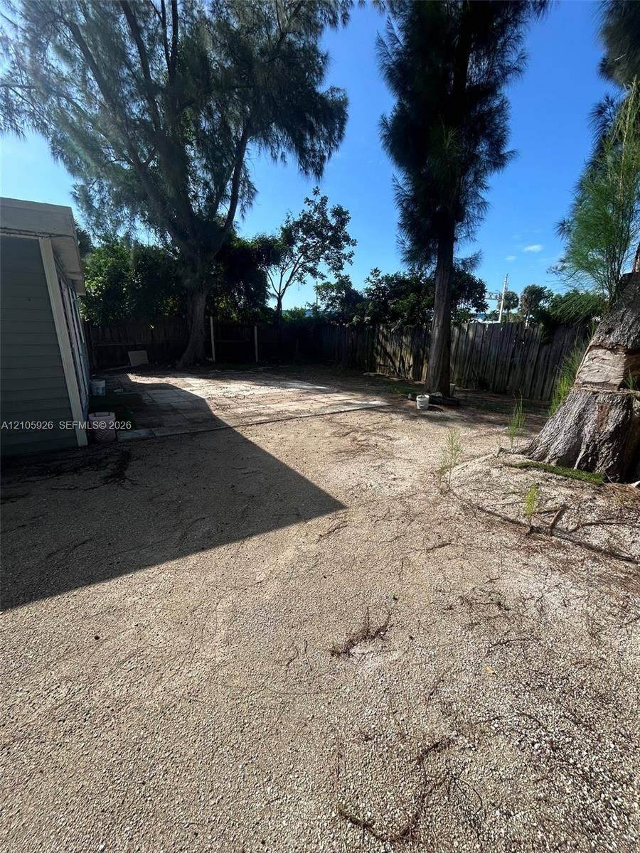 1601 W Avenue H W, Riviera Beach, Riviera Beach, FL 33404 Expansive backyard featuring a concrete patio, perimeter wood fencing, and mature trees