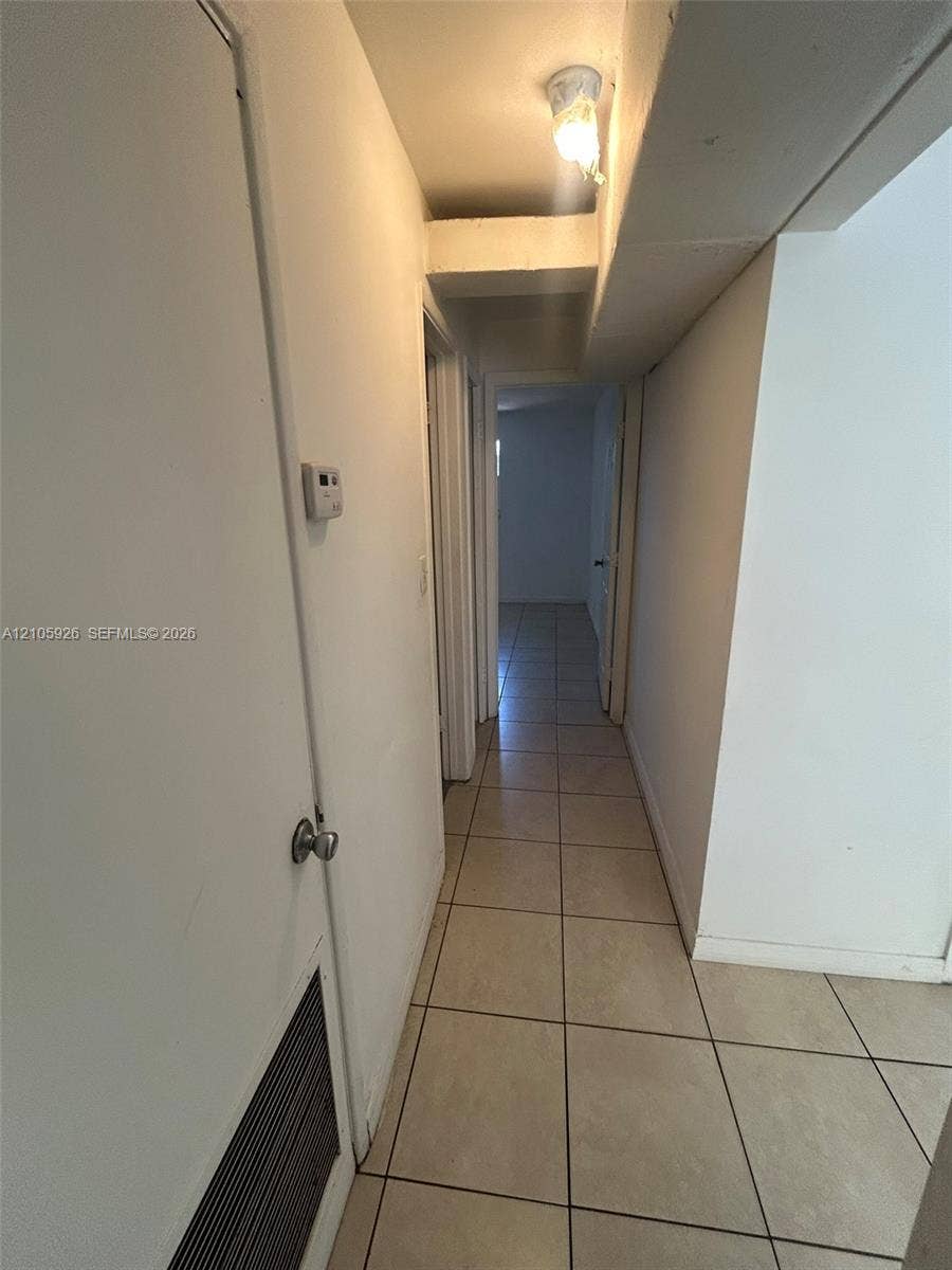 1601 W Avenue H W, Riviera Beach, Riviera Beach, FL 33404 Hallway featuring neutral-toned tile flooring, solid core interior doors, and a ceiling-mounted light fixture
