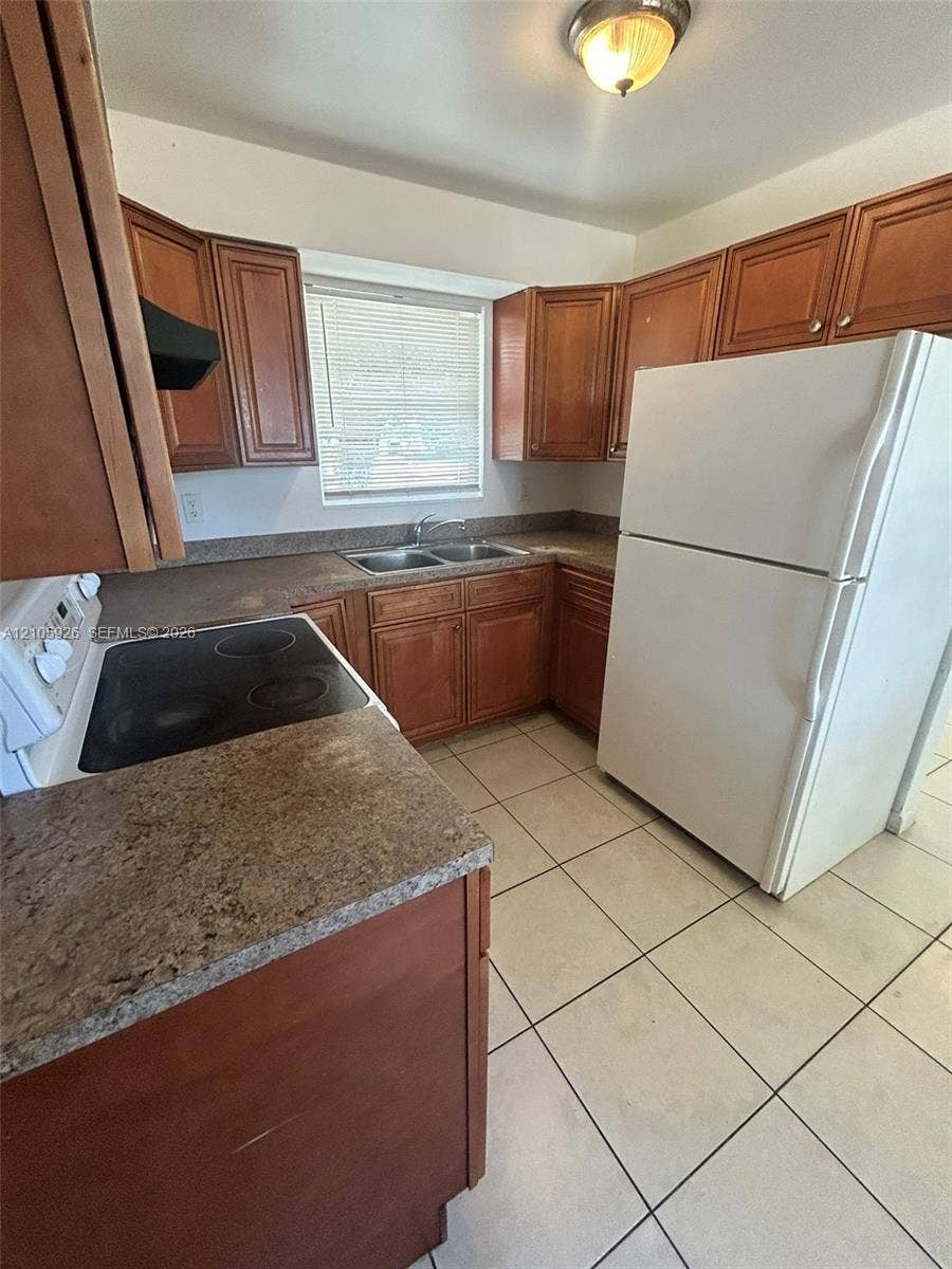 1601 W Avenue H W, Riviera Beach, Riviera Beach, FL 33404 Kitchen featuring wood cabinetry, stone-finish laminate countertops, ceramic tile flooring, a dual-basin stainless steel sink, and a flush-mount ceiling light fixture