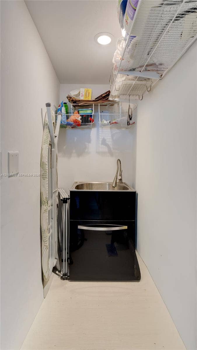 2655 Collins Avenue, #2301, Miami Beach, FL 33140 Utility area featuring a stainless steel drop-in sink, high-arc pull-down faucet, black cabinetry, and built-in wire shelving