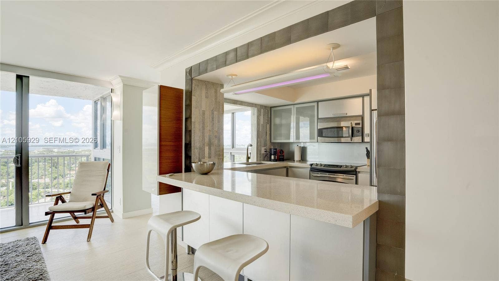 2655 Collins Avenue, #2301, Miami Beach, FL 33140 Kitchen featuring a stone-surface breakfast bar, glass-front cabinetry, stainless steel microwave, and metallic tile trim framing