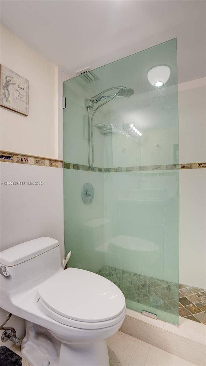 2655 Collins Avenue, #2301, Miami Beach, FL 33140 Walk-in shower featuring a frameless glass partition, wall-mounted rainfall showerhead, decorative tile border, and mosaic stone-finish floor