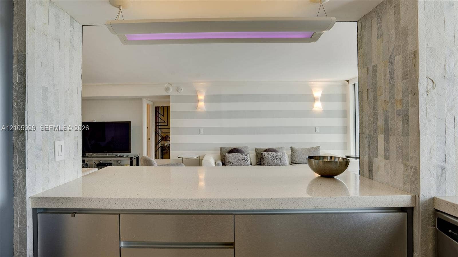 2655 Collins Avenue, #2301, Miami Beach, FL 33140 Kitchen island featuring solid-surface countertops, metallic-finish cabinetry, floor-to-ceiling textured stone wall accents, and custom overhead lighting