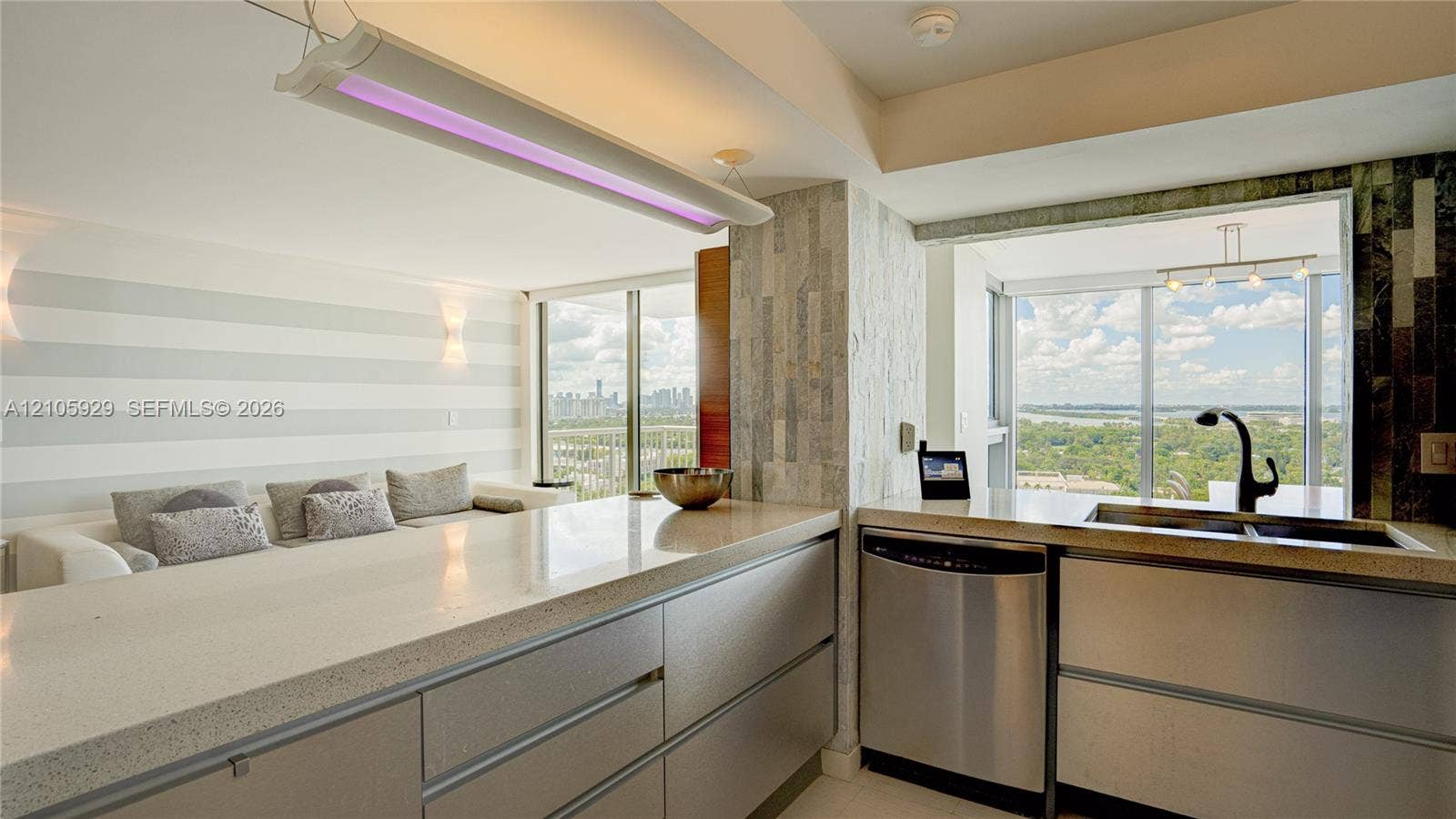 2655 Collins Avenue, #2301, Miami Beach, FL 33140 Kitchen featuring flat-panel cabinetry, light-toned stone-finish countertops, stainless steel appliances, a high-arc matte black faucet, and integrated linear lighting