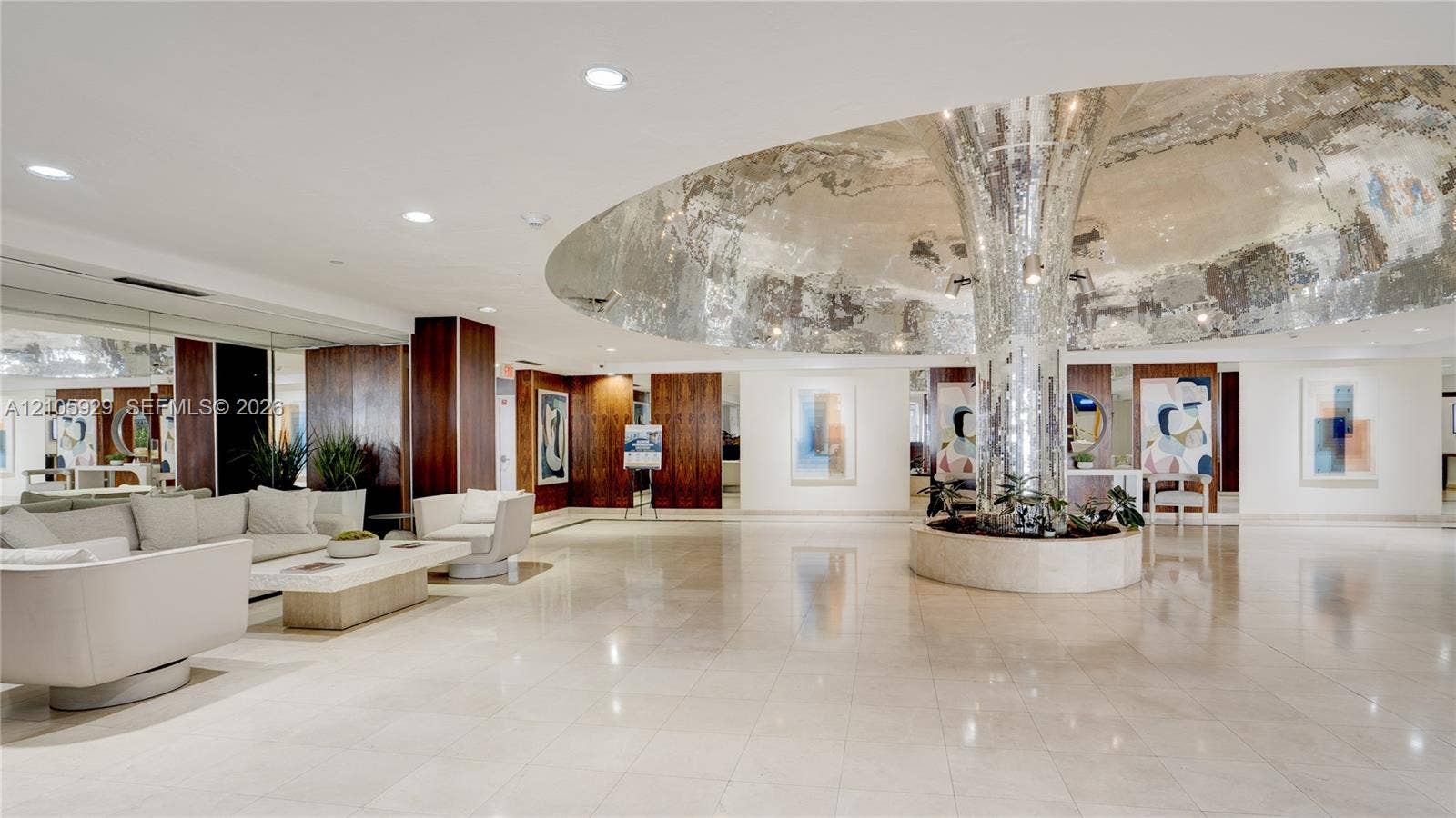 2655 Collins Avenue, #2301, Miami Beach, FL 33140 Grand lobby featuring polished stone flooring, a mirrored central structural column, recessed ceiling lighting, and wood-paneled wall accents